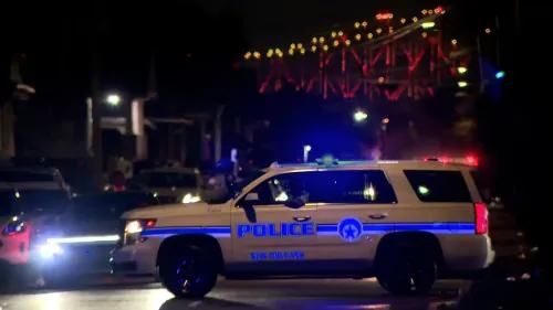 سيارة شرطة نيو أورليانز مزودة بأضواء متلألئة، متوقفة في موقع حادث إطلاق نار خلال موكب شعبي، مع خلفية جسر مضاء.