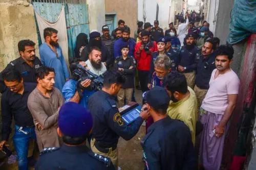 مجموعة من الأشخاص في شارع ضيق، بينهم رجال شرطة وصحفيون، يتجمعون حول شخص يتحدث إلى ضابط شرطة، مما يبرز التوتر الاجتماعي في المنطقة.