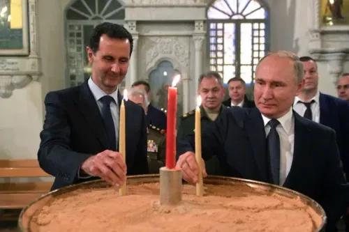 بشار الأسد وفلاديمير بوتين يضيئان الشموع في كنيسة، مع وجود مسؤولين آخرين في الخلفية، في سياق الأحداث السياسية في سوريا.