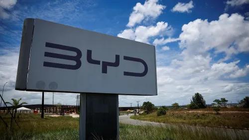 لافتة كبيرة تحمل شعار شركة BYD في موقع بناء مصنع جديد في البرازيل، مع سماء زرقاء وسحب بيضاء في الخلفية.