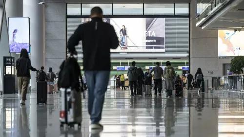 مطار حديث مزدحم بالمسافرين الذين يحملون حقائبهم، مع لافتات إعلانات ترويجية في الخلفية، تعكس جهود الصين لجذب السياح الأجانب.