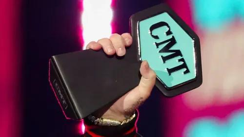 يد تظهر جائزة CMT Music Awards، مع خلفية ملونة، تعكس أجواء الحفل المبهجة والترشيحات المتعددة للفنانين.