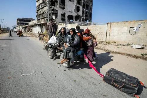 عائلة فلسطينية تجلس على عربة تجرها حيوانات، محملة بأمتعة، في شارع في شمال غزة، خلفهم مبنى مدمر.