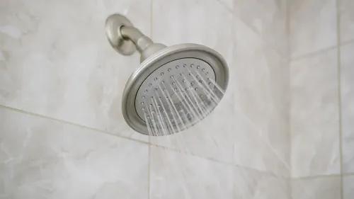 رأس الدش يتدفق منه الماء، مما يعكس موضوع المقال حول التبول أثناء الاستحمام وتأثيراته الصحية.