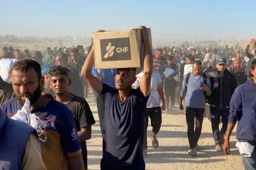 مواطن يحمل صندوق مساعدات من مؤسسة GHF وسط حشود من الأشخاص في غزة، يعكس مشهد التوتر والبحث عن المساعدة الإنسانية.