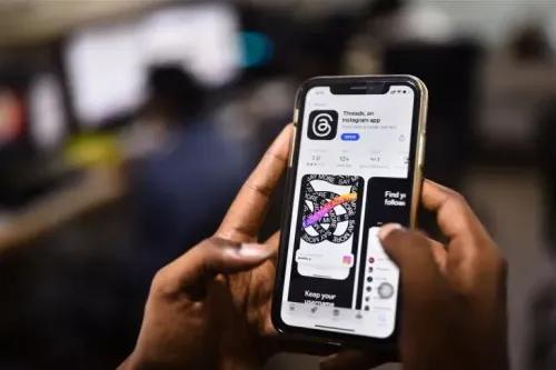شخص يستخدم هاتفًا ذكيًا لعرض تطبيق \"Threads\" الخاص بإنستغرام، مع التركيز على واجهة المستخدم والتفاعلات الاجتماعية.