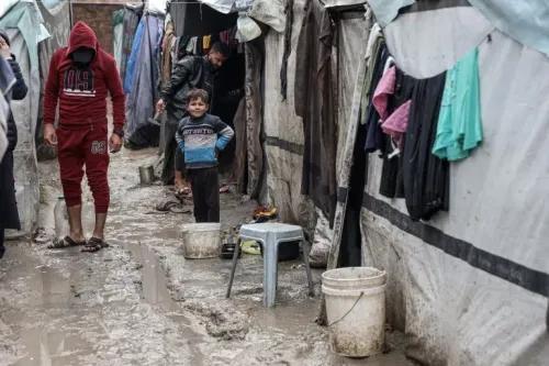 أطفال فلسطينيون في مخيم للاجئين بغزة، وسط ظروف معيشية صعبة، حيث تتساقط الأمطار على الخيام المتهالكة.