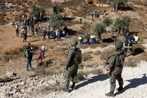 مجموعة من الأشخاص في منطقة زراعية، مع وجود جنود إسرائيليين يراقبون الوضع، مما يعكس التوترات المستمرة في فلسطين.