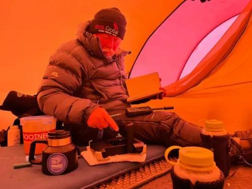 عالم المناخ آلان تشامبرز يجلس في خيمة برتقالية، يكتب ملاحظات ويستخدم معدات بحثية خلال استكشافه في القارة القطبية الجنوبية.