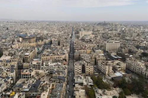 منظر جوي لمدينة حمص السورية، يظهر المباني المتضررة والشوارع المزدحمة، في سياق الصراع المستمر وتأثيره على المدنيين.