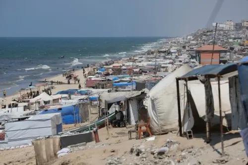 شاطئ الزوايدة مزدحم بخيام اللاجئين، حيث يعيش الناس في ظروف قاسية، مع البحر في الخلفية، مما يعكس معاناة الحرب.
