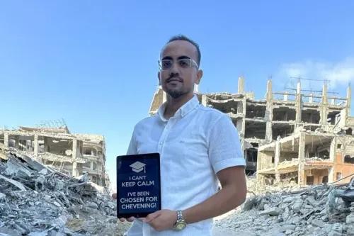 شاب يحمل لوحة مكتوب عليها \"لا أستطيع الحفاظ على هدوئي. لقد تم اختياري في تشيفنينج!\"، يقف أمام أنقاض مبنى في غزة.