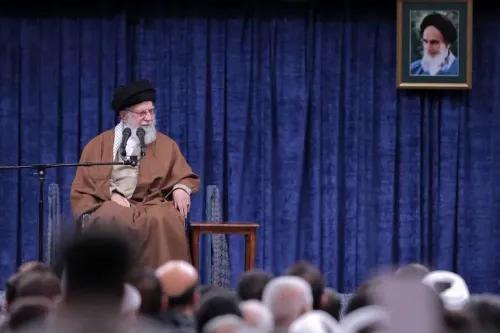 خامنئي يتحدث خلال خطاب في طهران، متهمًا الولايات المتحدة وإسرائيل بالتآمر للإطاحة بالأسد، مع صورة له على الجدار خلفه.