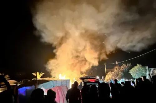 سحب من الدخان تتصاعد في السماء وسط تجمع حشود من الناس بعد هجوم إسرائيلي على مخيم للاجئين في غزة، مما يعكس تصعيد العنف.