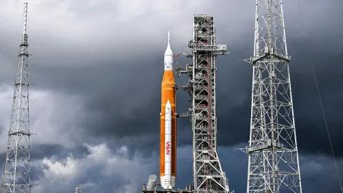 صاروخ SLS التابع لناسا، ذو اللون البرتقالي، واقفًا على منصة الإطلاق تحت سماء غائمة، يمثل جزءًا أساسيًا من برنامج أرتميس لاستكشاف القمر.