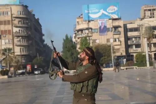 مقاتل من المعارضة السورية يحمل سلاحه في ساحة حلب، مع خلفية لمبانٍ وأعلام، مشيراً إلى تصاعد النشاط العسكري في المنطقة.