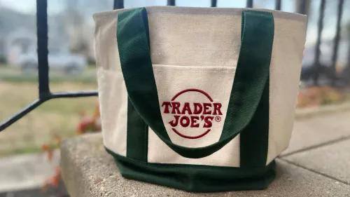 حقيبة قماشية من Trader Joe's بتصميم بسيط، تحمل شعار المتجر، موضوعة على سطح خرساني، تعكس اتجاه المنتجات الصغيرة في السوق.