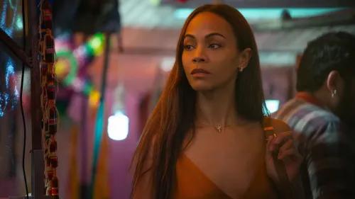 ريتا، التي تؤديها زوي سالدانا، تظهر في مشهد من فيلم \"إميليا بيريز\"، حيث تعكس تعبيرات وجهها التوتر والقلق في بيئة ملونة.