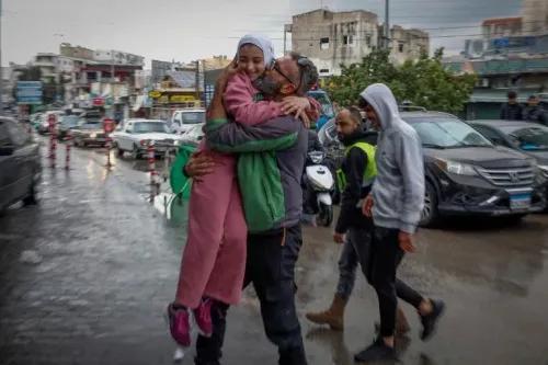 طفلة صغيرة في معطف وردي تُحتضن من قبل رجل مبتسم في الشارع المزدحم، حيث تعود العائلات إلى منازلها بعد وقف إطلاق النار في لبنان.